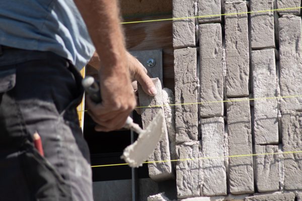 close-up Builder glues a gray brick with cement to the masonry on the facade of a new house. High quality photo