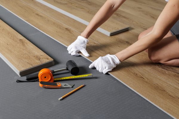Close view of hands aligning SPC vinyl plank on underlayment with tools and tape for home renovation